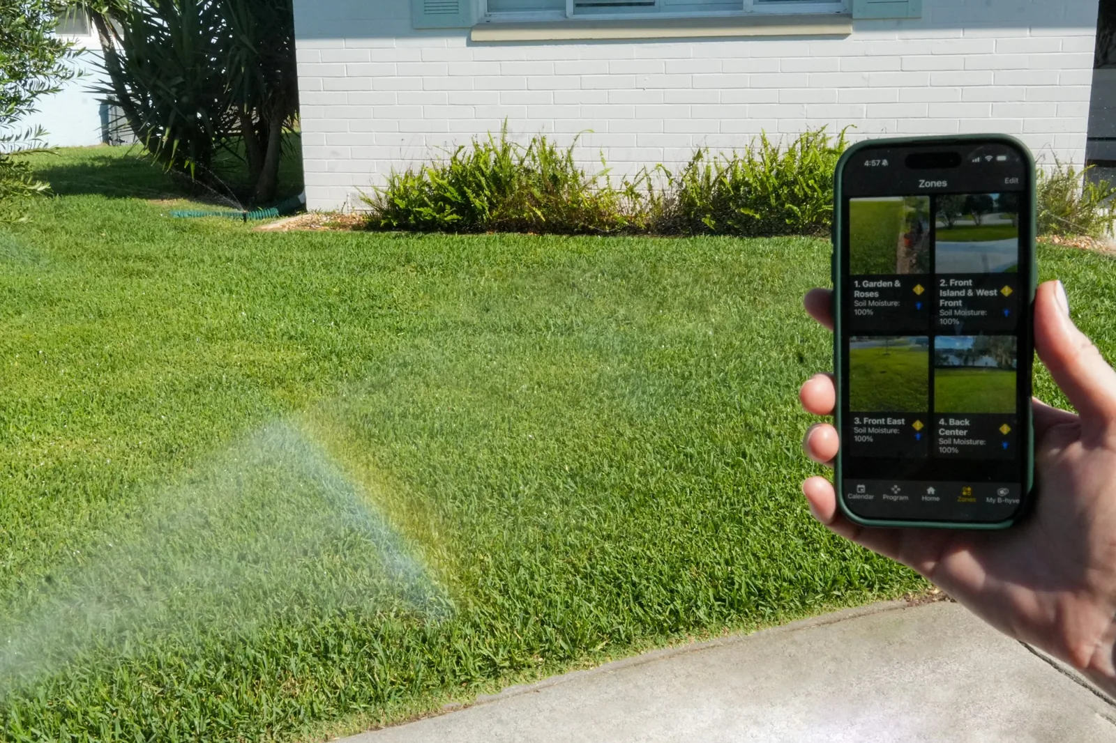 Homeowner controlling a WaterCare-installed irrigation system from a smartphone app while a zone runs behind