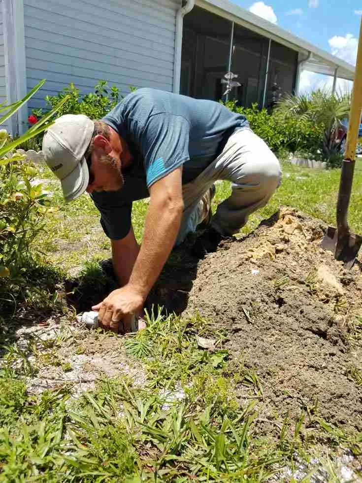 WaterCare technician repairing a buried sprinkler head in an excavated lawn area